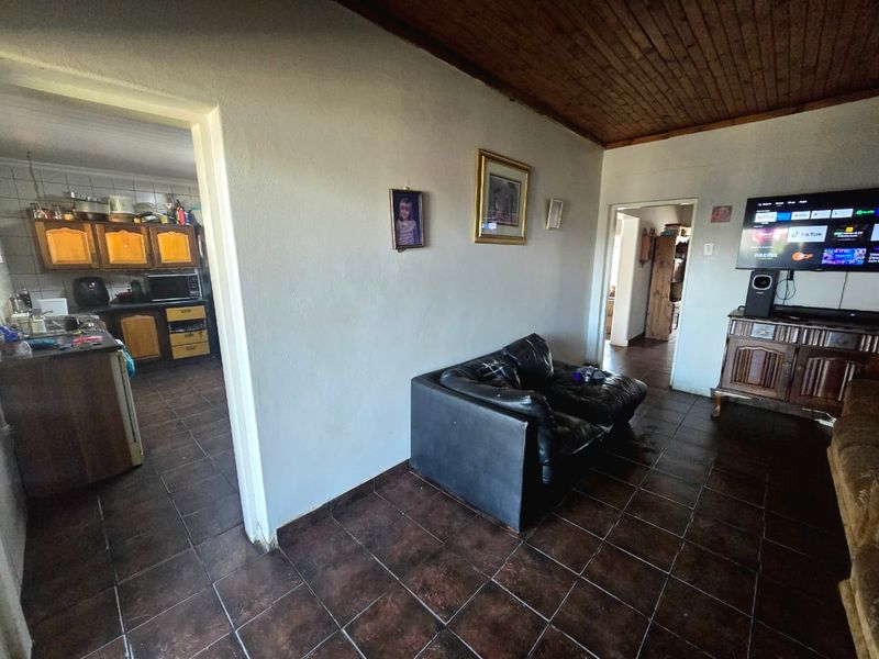 Open plan living area featuring tiled flooring and timber ceiling, with an adjacent kitchen space visible through the doorway.