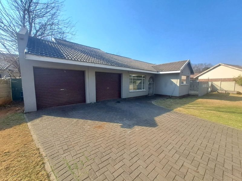 Front view of a single-story house featuring a double garage, paved driveway, and tiled roof, set on a residential plot.