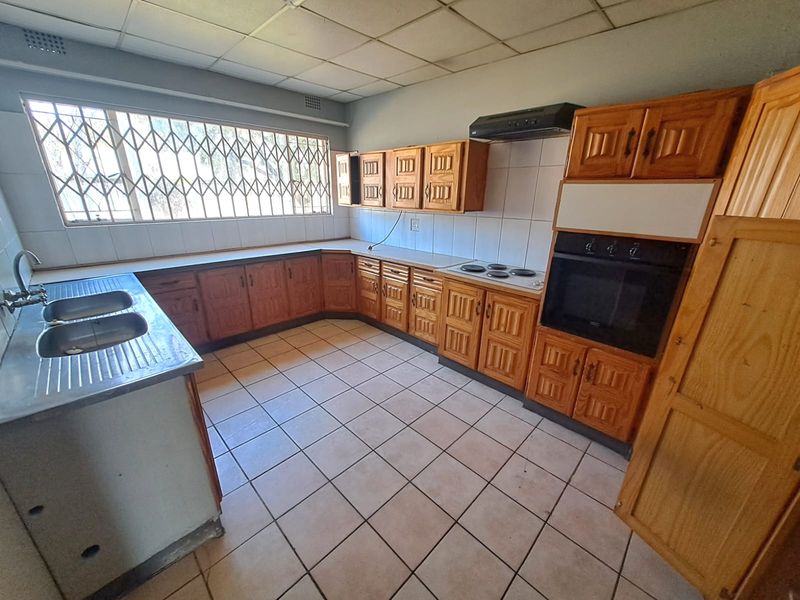 A dated kitchen featuring wooden cabinetry, built-in oven, electric hob, and tiled flooring, offering a functional layout ready for modernization.