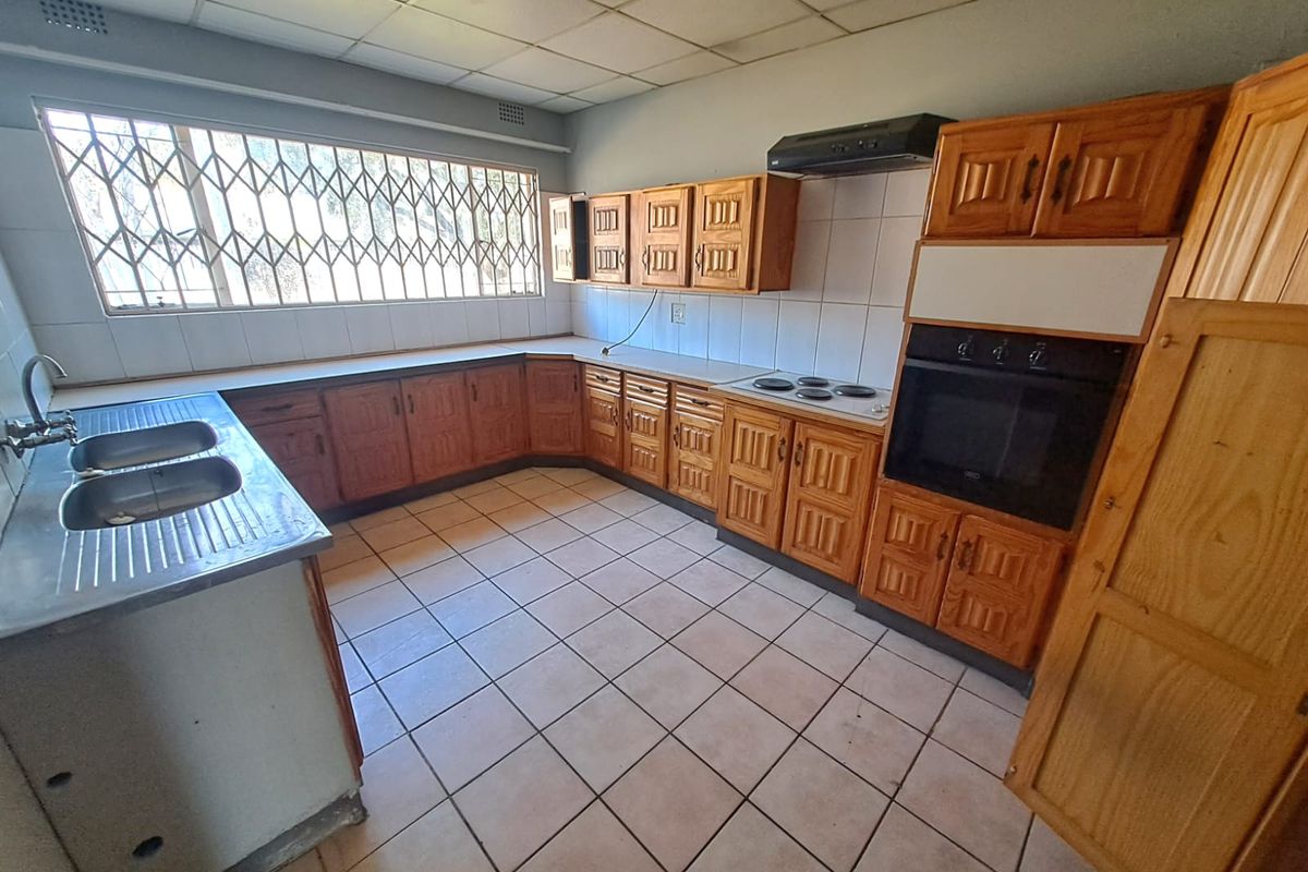 A dated kitchen featuring wooden cabinetry, built-in oven, electric hob, and tiled flooring, offering a functional layout ready for modernization.