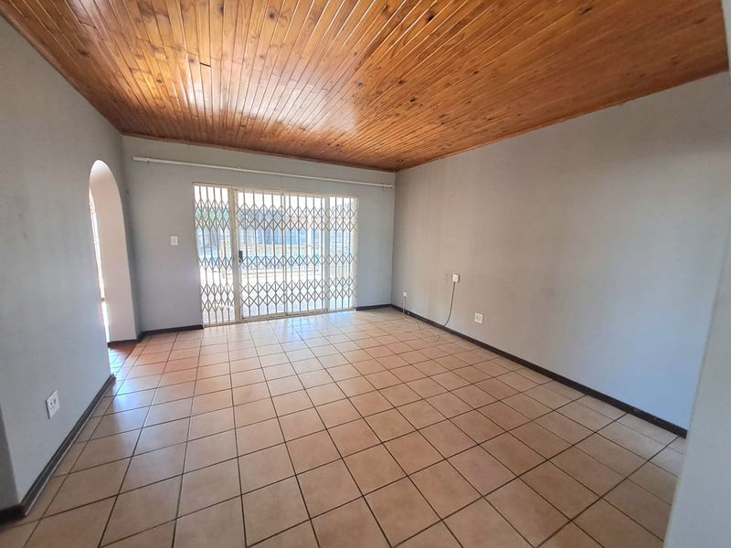 Spacious living area featuring ceramic floor tiles, a timber tongue and groove ceiling, and a sliding glass door with a security gate.