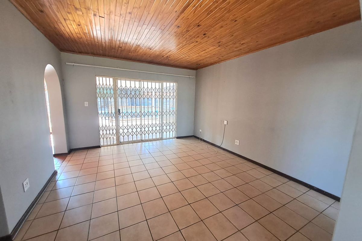 Spacious living area featuring ceramic floor tiles, a timber tongue and groove ceiling, and a sliding glass door with a security gate.