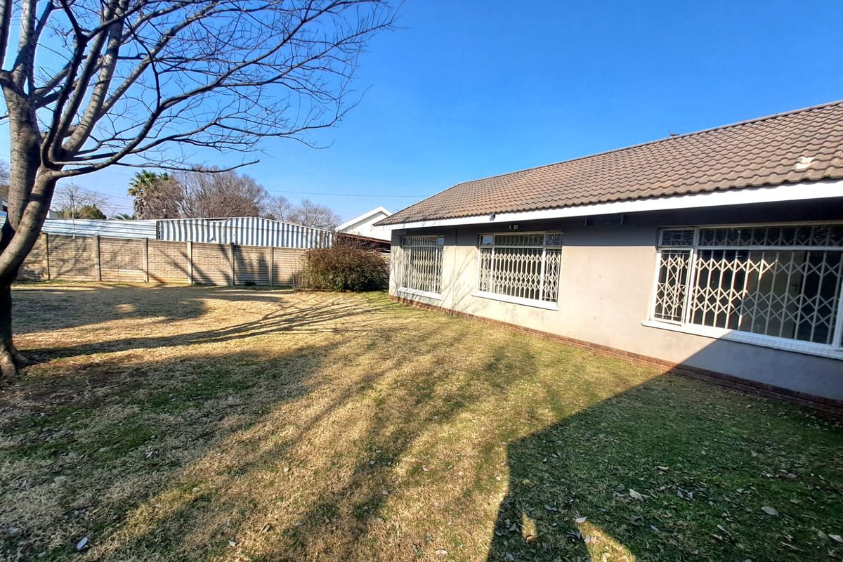 Rear view of the property featuring a tiled roof, security gates on windows, and a spacious garden area with a precast concrete boundary wall.