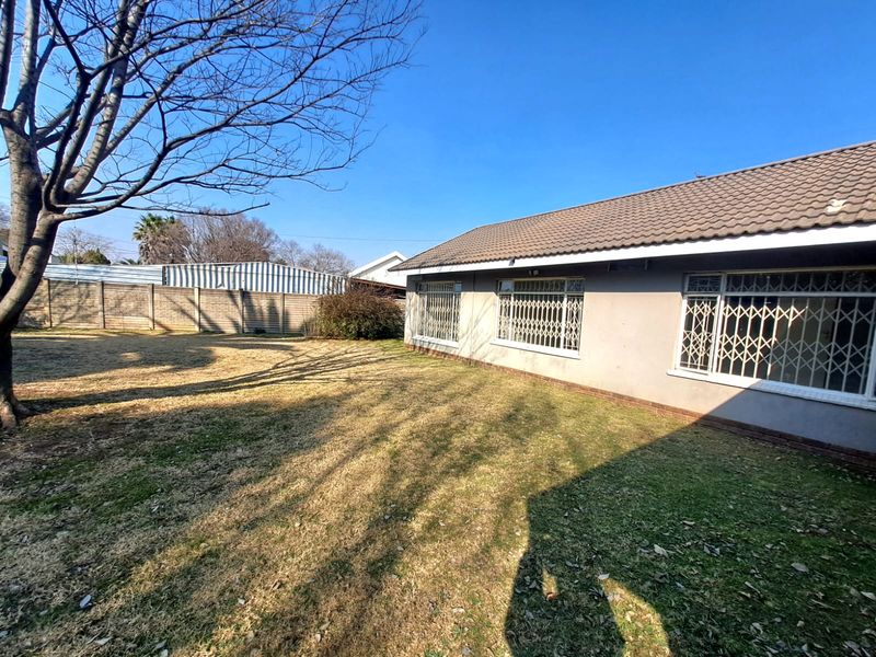 Rear view of the property featuring a tiled roof, security gates on windows, and a spacious garden area with a precast concrete boundary wall.