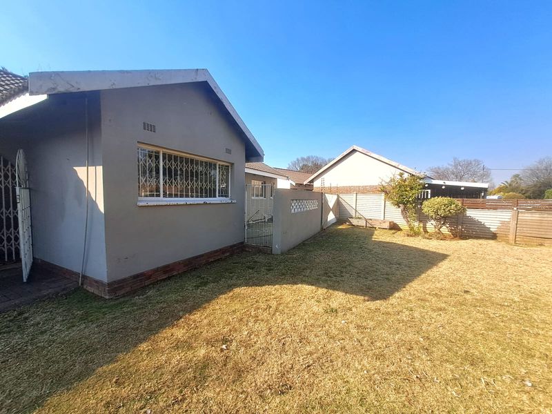 Rear exterior view of the house featuring a lawn, security bars on windows, and perimeter precast concrete walling with electric fencing.