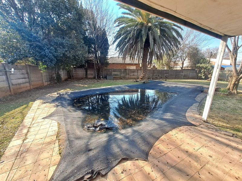 Outdoor pool area featuring a paved patio, a swimming pool with a protective cover, and a surrounding garden with boundary walling.