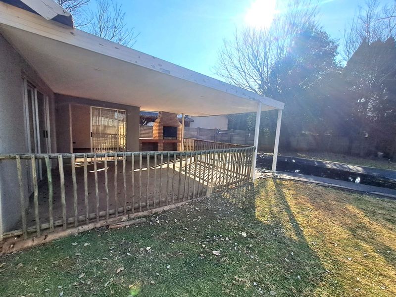 Covered outdoor patio featuring a built-in brick braai, wooden balustrade, and direct access to the garden and pool area.