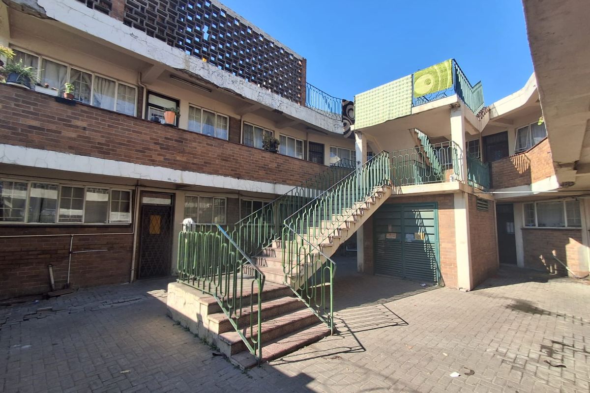 A view of the rear courtyard featuring a brick facade, external concrete staircase with metal railings, and paved ground area.