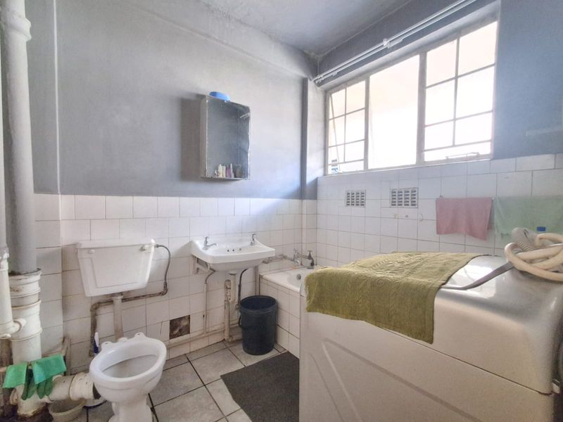 A dated bathroom featuring a standard toilet, washbasin, and bathtub with tiled finishes, requiring modernization and cosmetic updates.