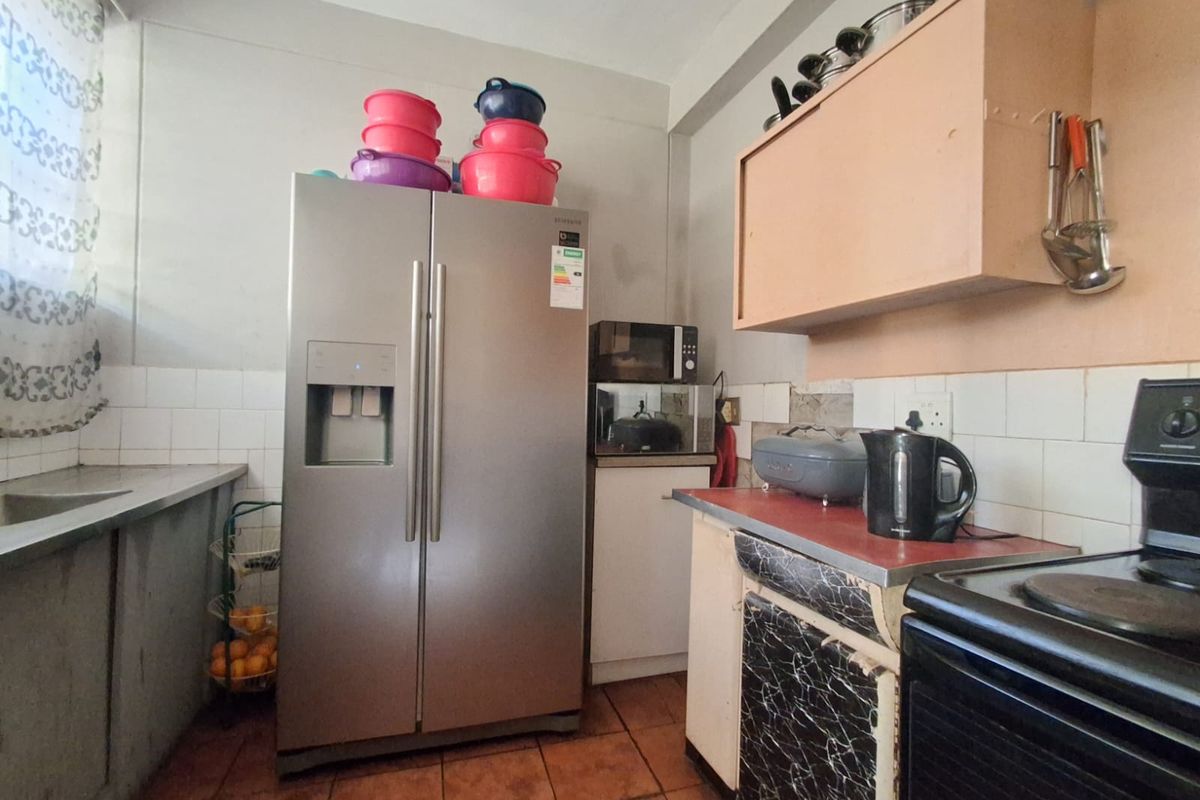 A functional kitchen featuring tiled flooring, a tiled splashback, and built-in cabinetry with a laminate countertop and stainless steel sink.