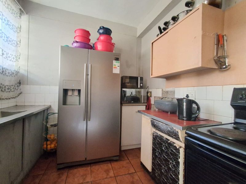 A functional kitchen featuring tiled flooring, a tiled splashback, and built-in cabinetry with a laminate countertop and stainless steel sink.