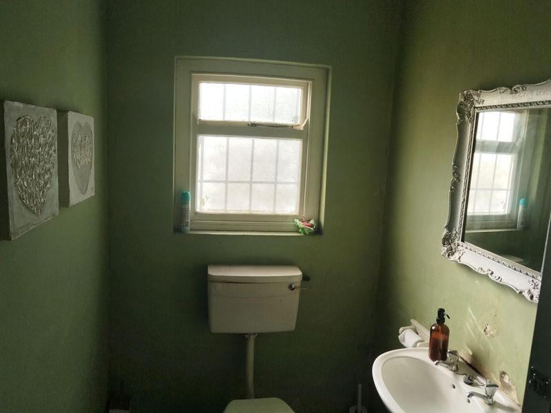 A small bathroom featuring a standard toilet and wall-mounted washbasin, requiring cosmetic updates to the wall finishes.