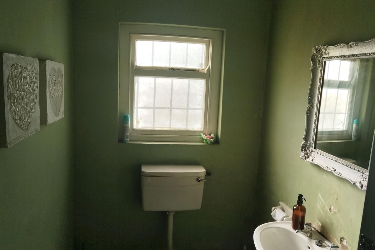 A small bathroom featuring a standard toilet and wall-mounted washbasin, requiring cosmetic updates to the wall finishes.