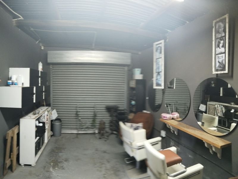 A converted garage space currently utilized as a salon, featuring a roller shutter door, built-in shelving, and wall-mounted mirrors.