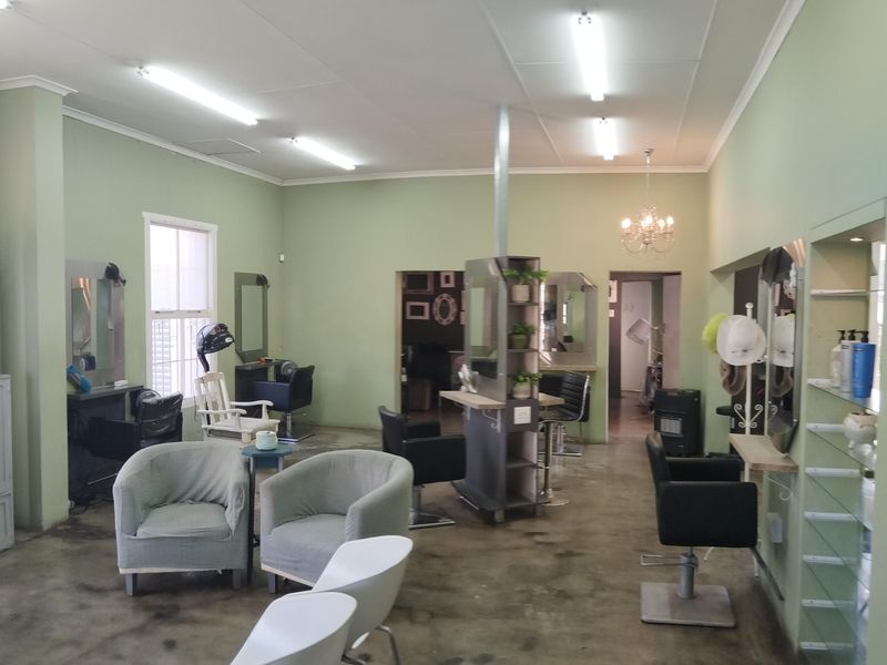 A commercial salon space featuring polished concrete floors, fluorescent lighting, and built-in shelving units, currently configured for hair styling services.