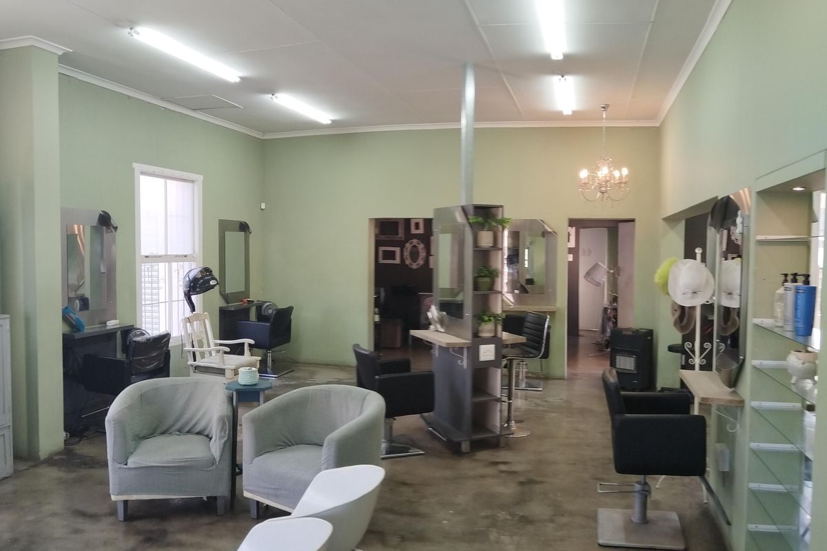 A commercial salon space featuring polished concrete floors, fluorescent lighting, and built-in shelving units, currently configured for hair styling services.