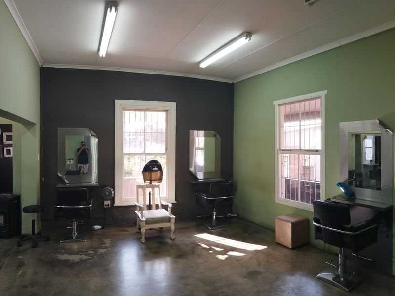A commercial utility space currently configured as a salon, featuring concrete floors, sash windows with security bars, and fluorescent lighting.