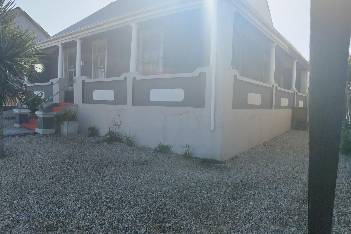 Front elevation of a house featuring a covered veranda with decorative columns, security bars on windows, and a gravel driveway.