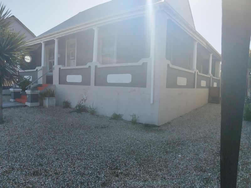 Front elevation of a house featuring a covered veranda with decorative columns, security bars on windows, and a gravel driveway.