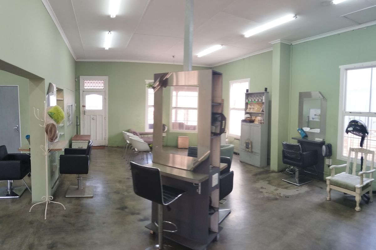 A commercial-style interior space featuring concrete flooring, fluorescent lighting, and multiple window points, currently configured as a salon.