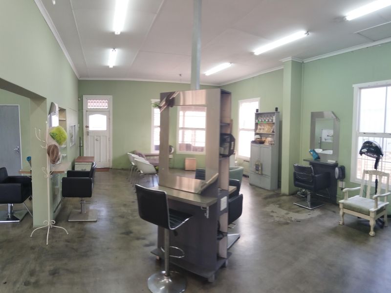 A commercial-style interior space featuring concrete flooring, fluorescent lighting, and multiple window points, currently configured as a salon.