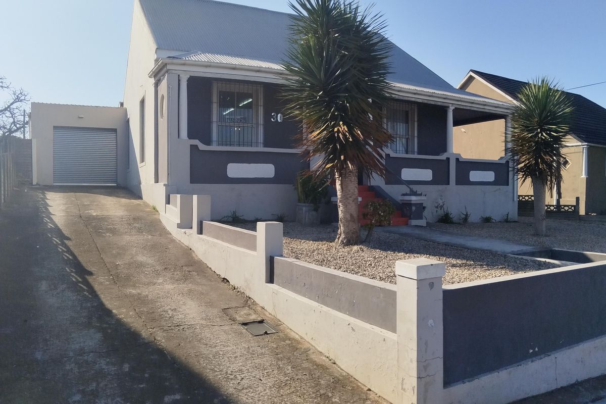 Front elevation of a single-story house featuring a corrugated metal roof, concrete driveway, attached garage, and a covered front porch with security window bars.