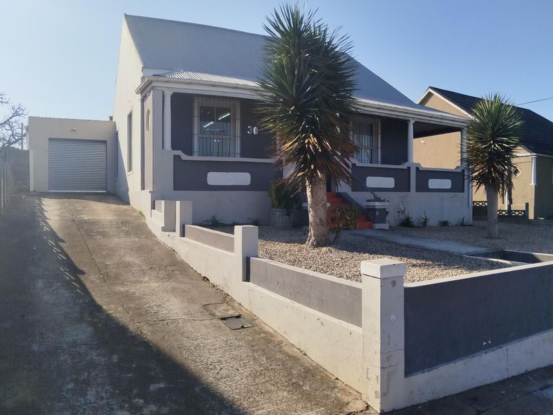 Front elevation of a single-story house featuring a corrugated metal roof, concrete driveway, attached garage, and a covered front porch with security window bars.