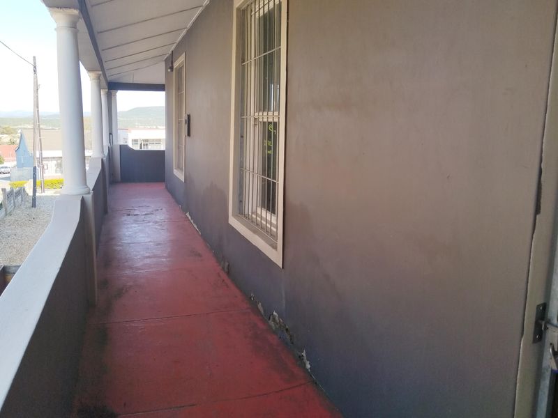 A covered balcony featuring concrete columns, security-barred windows, and a painted concrete floor, showing signs of wear and plaster damage at the wall base.