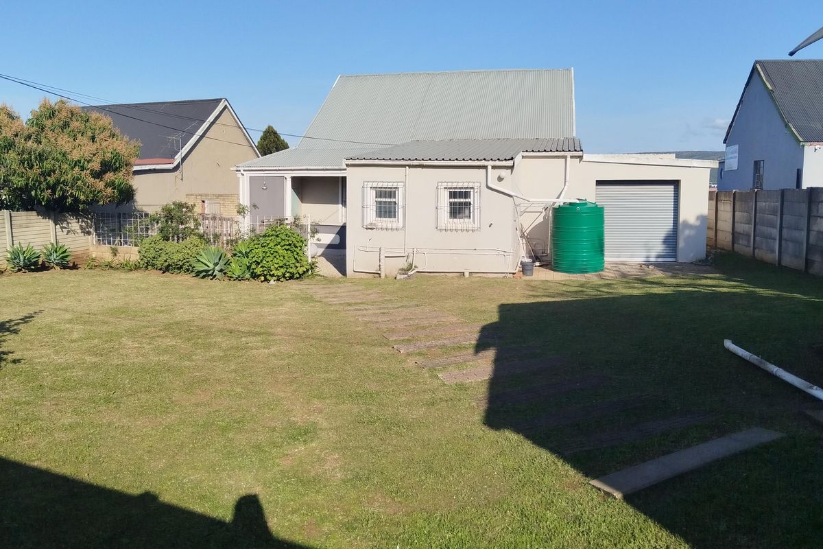 Rear view of the property featuring a spacious lawn, corrugated metal roof, integrated garage, and a water storage tank.
