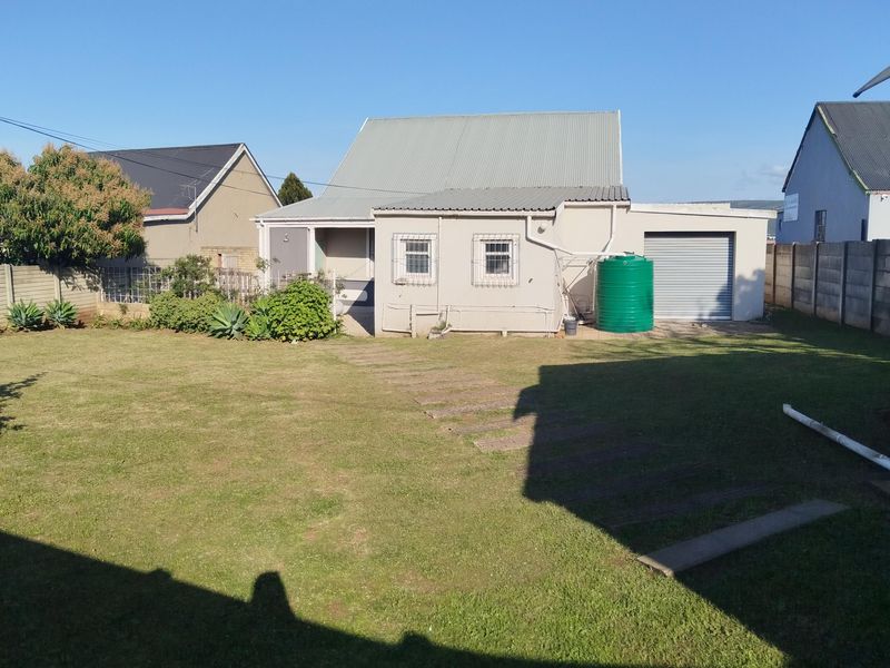 Rear view of the property featuring a spacious lawn, corrugated metal roof, integrated garage, and a water storage tank.