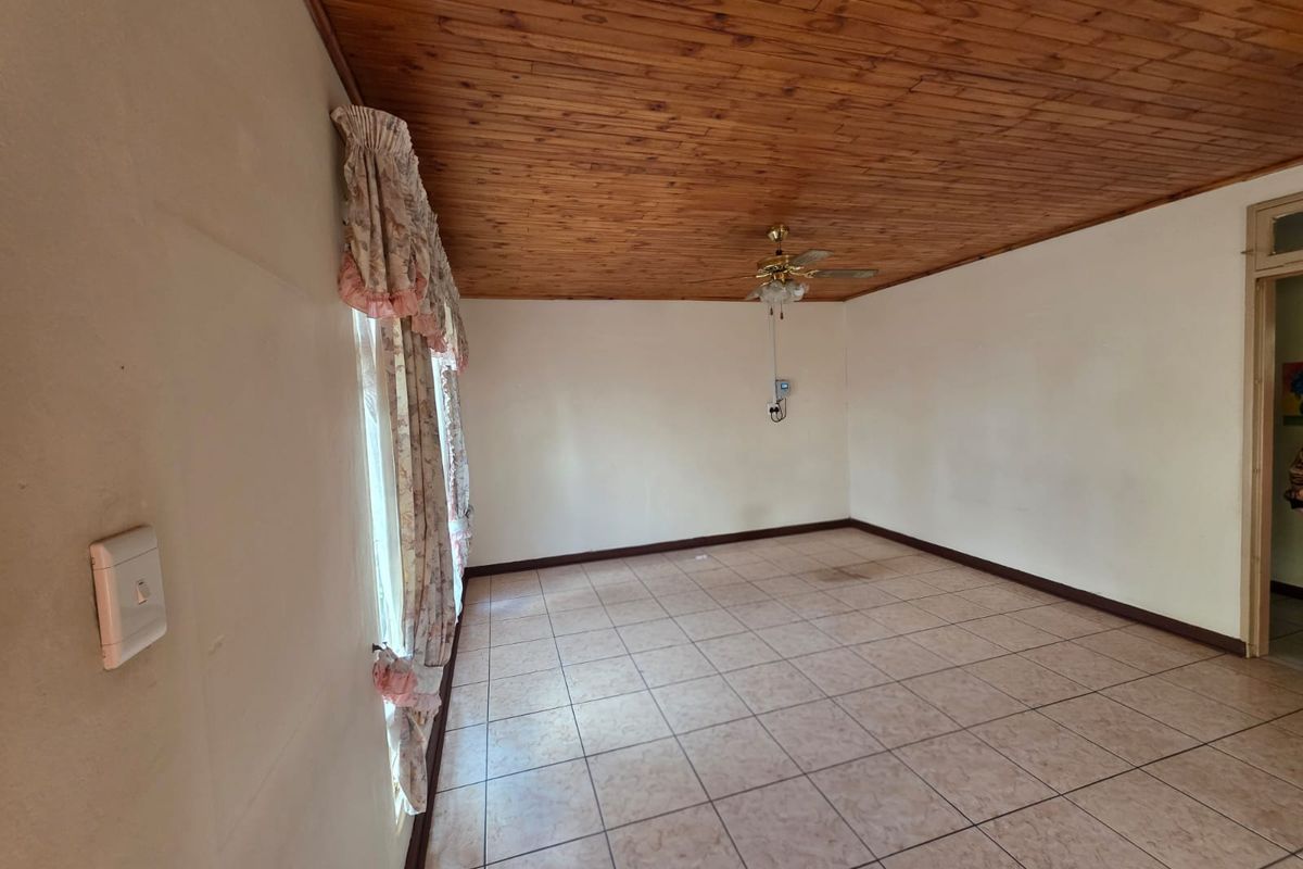 An empty living room featuring a timber-clad ceiling, ceiling fan, and tiled flooring, offering a blank canvas for renovation.
