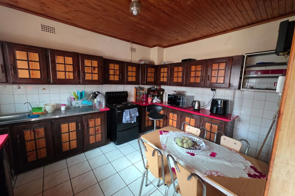 A functional kitchen featuring dark wood cabinetry, tiled backsplash, and tiled flooring, with a wooden ceiling and integrated dining space.