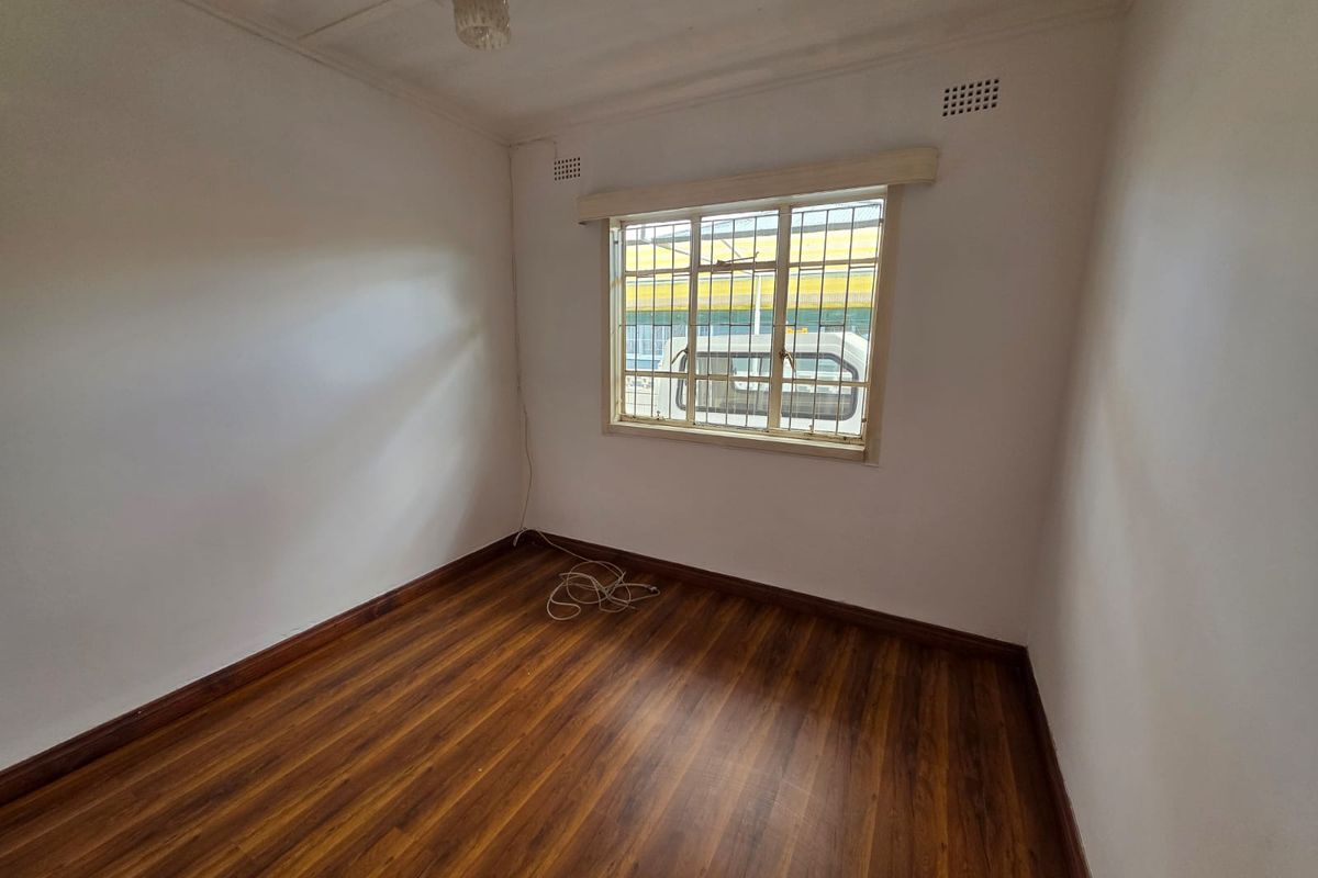 An empty bedroom featuring laminate wood-look flooring, white walls, and a window fitted with security bars.