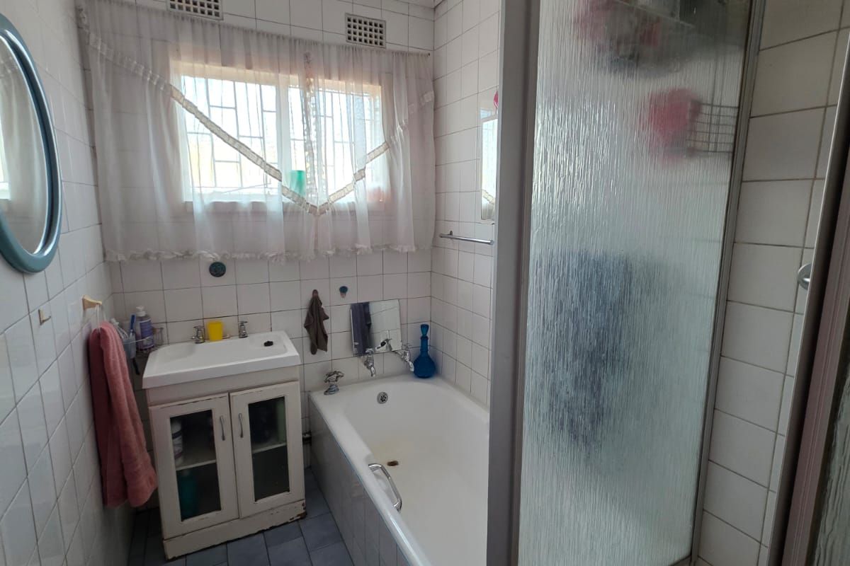 A functional bathroom featuring a bathtub, separate shower enclosure, and vanity basin with tiled finishes throughout.