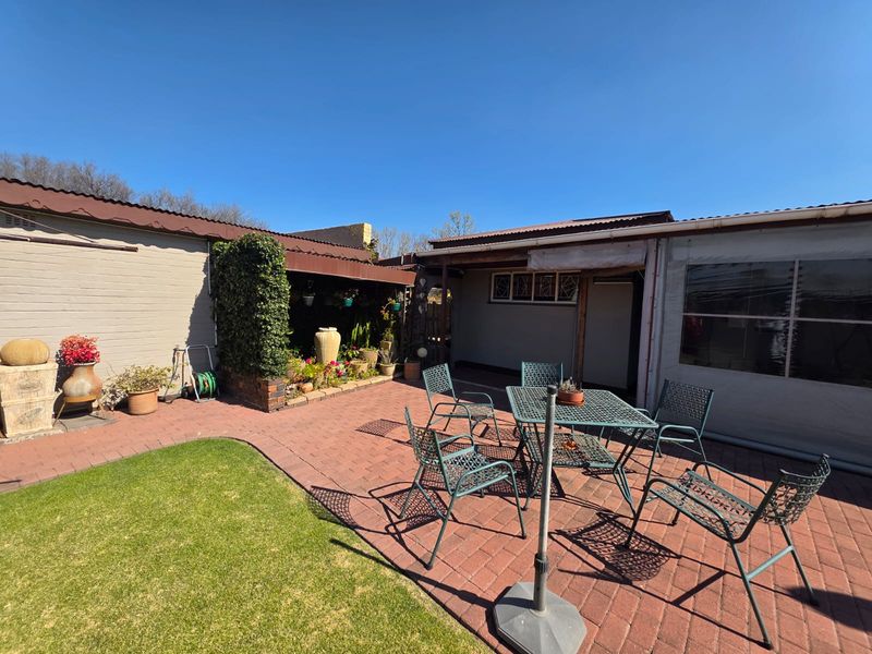 A paved outdoor patio area featuring a covered section and direct access to the garden, providing a functional space for outdoor living.