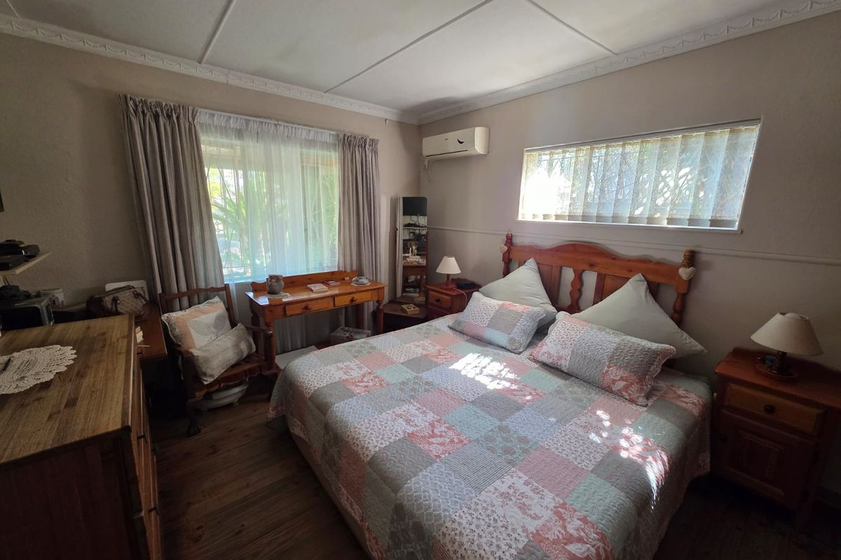 A cozy bedroom featuring timber flooring, decorative ceiling cornices, and a wall-mounted split-system air conditioner for climate control.
