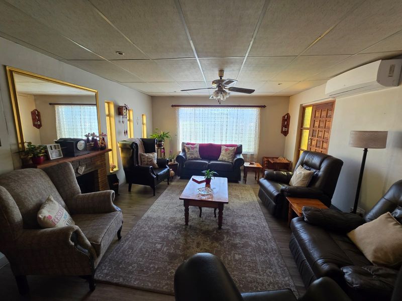 A spacious living room featuring a fireplace, ceiling fan, and split-system air conditioning unit, finished with laminate flooring and a drop-ceiling.