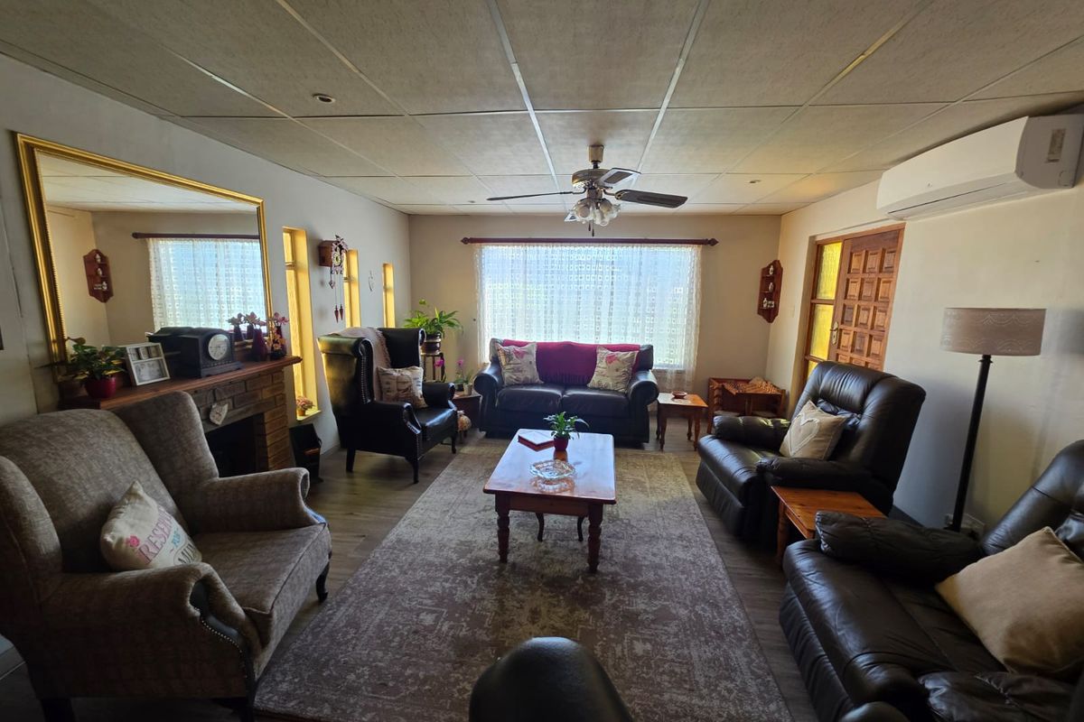 A spacious living room featuring a fireplace, ceiling fan, and split-system air conditioning unit, finished with laminate flooring and a drop-ceiling.