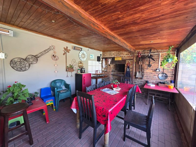 Covered outdoor patio featuring a timber ceiling, brick flooring, and a built-in braai, providing a functional space for outdoor dining and entertainment.