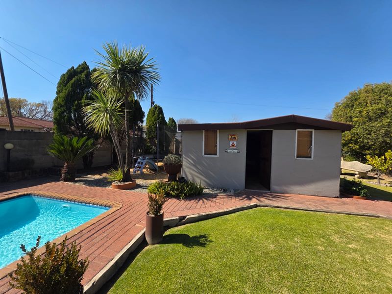 A well-maintained outdoor pool area featuring brick paving, a manicured lawn, and a detached utility shed in the garden.