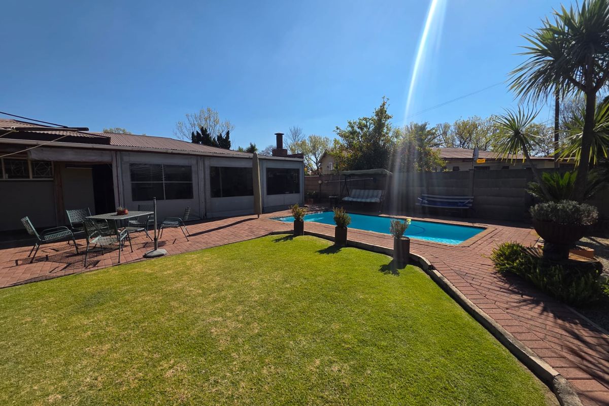 Rear garden area featuring a swimming pool, paved patio space, and established lawn, enclosed by a brick boundary wall.