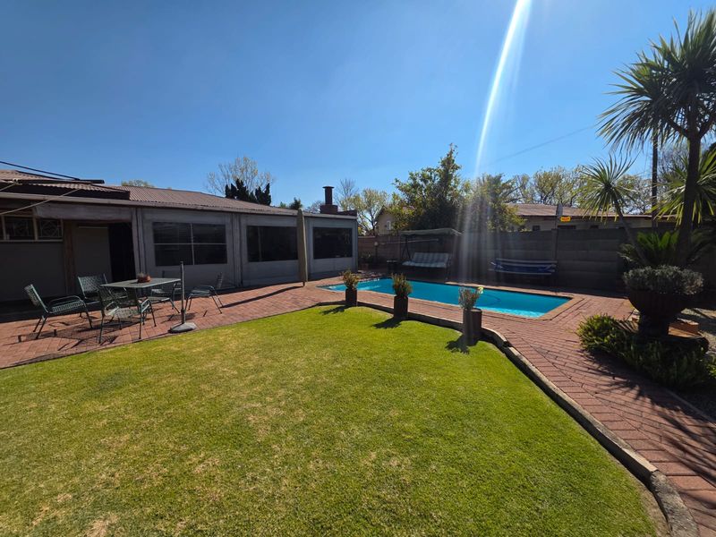 Rear garden area featuring a swimming pool, paved patio space, and established lawn, enclosed by a brick boundary wall.