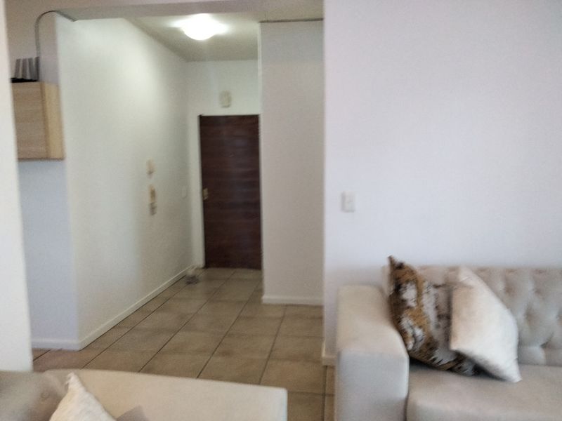 An entry area featuring tiled flooring and a solid wood entrance door, leading into the main living space of the flat.