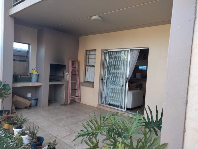 Covered patio area featuring a built-in braai, tiled flooring, and direct access to the interior living space through a sliding door with security gate.