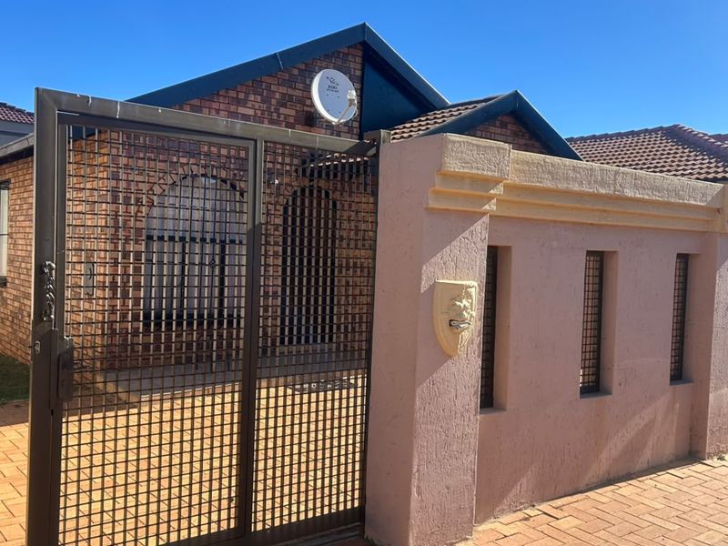 Front view of a face brick house featuring a secure metal gate, perimeter wall, and tiled roof.
