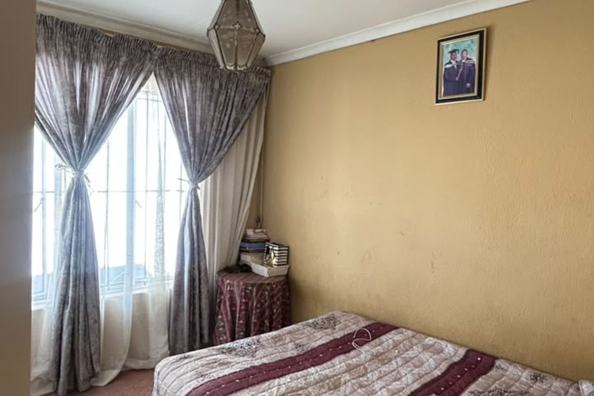 A bedroom featuring a window with security bars, coving, and a pendant light fixture. The room requires cosmetic updates to the walls and ceiling.