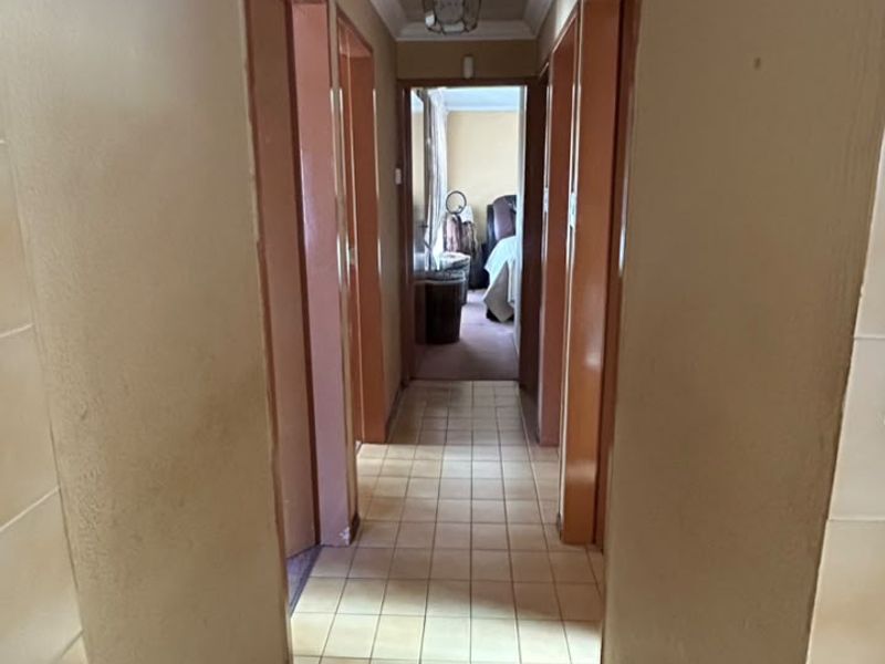 A narrow residential hallway featuring tiled flooring, coved ceilings, and multiple doorways leading to adjacent rooms.