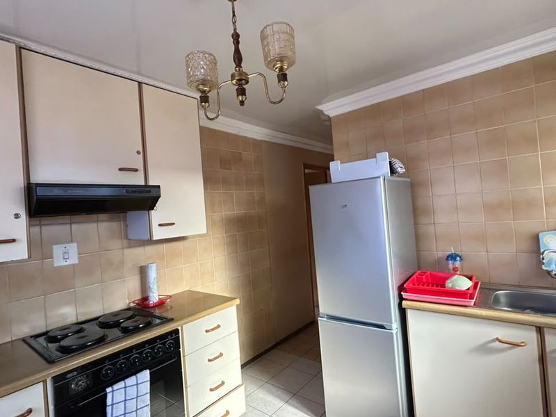 A functional kitchen featuring built-in cabinetry, an electric hob with extractor fan, and a double sink with tiled splashbacks.