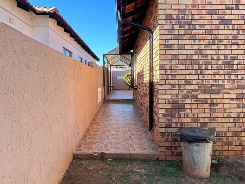 A side walkway featuring brick exterior walls, tiled flooring, and functional guttering, leading towards the rear of the property.