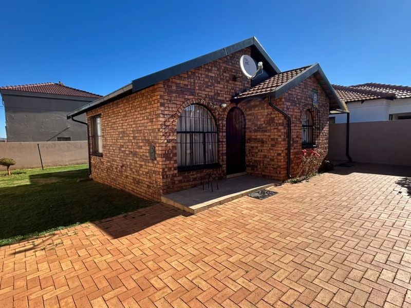 A well-maintained face-brick house featuring a paved driveway, secure window bars, and a tiled roof, set within a neat residential plot.
